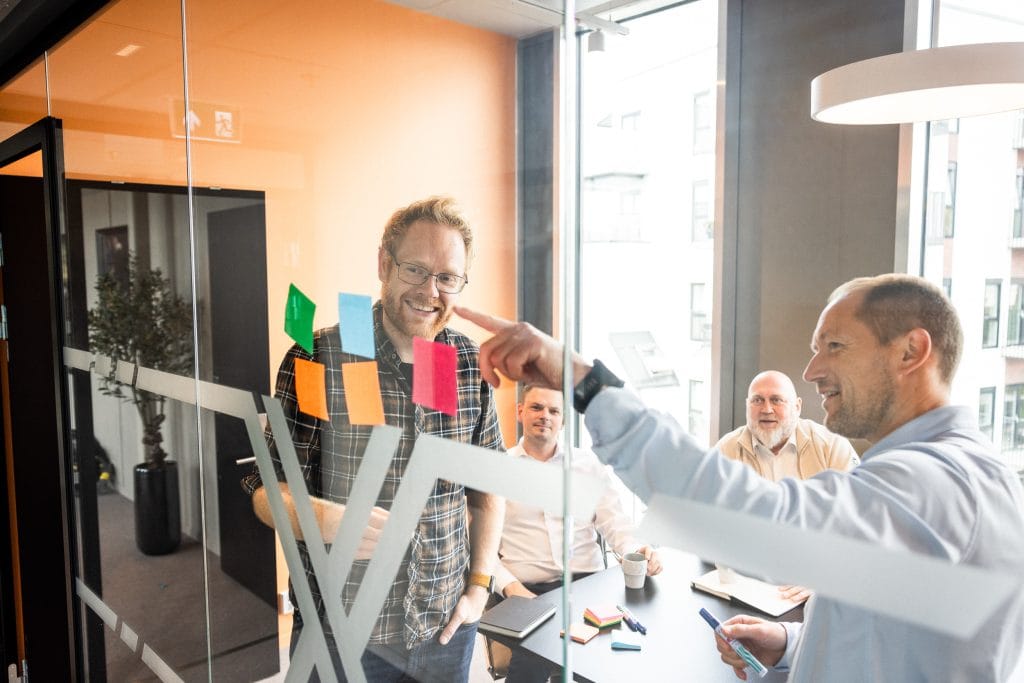 Notatlapper på et innvendig kontorvindu og ansatte som står rundt